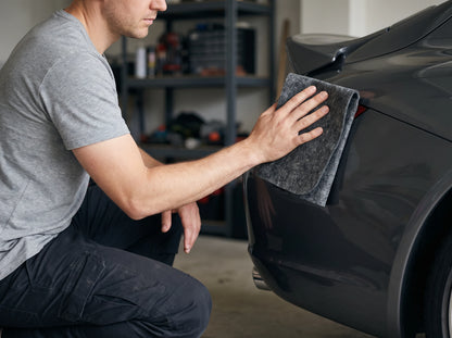 Man crouching in a garage, holding the NanoPolix Nano Sparkle Cloth against the rear corner of a dark gray car